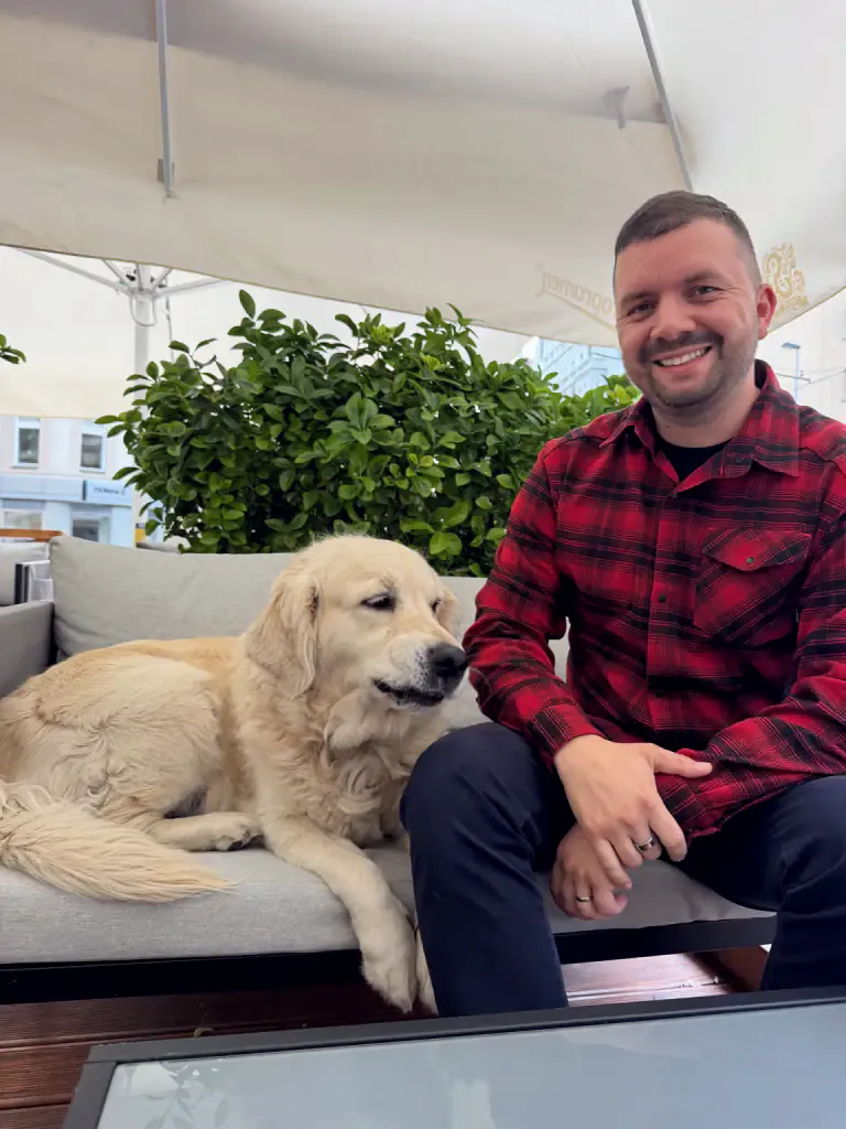 Peter sedí na terase a usmieva sa, vedľa neho leží Tiffany, zlatá retríverka